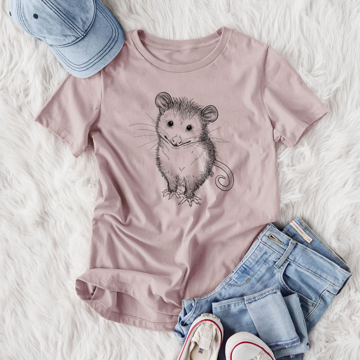 Women's relaxed fit cotton t-shirt printed with a black ink illustration of a wide-eyed baby opossum sitting, styled flat on a white faux fur rug with jeans.