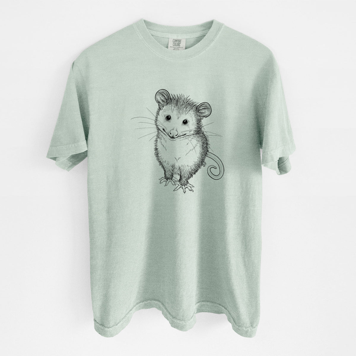 Bay green Comfort Colors t-shirt laid flat, printed with a black ink illustration of a wide-eyed baby opossum sitting.