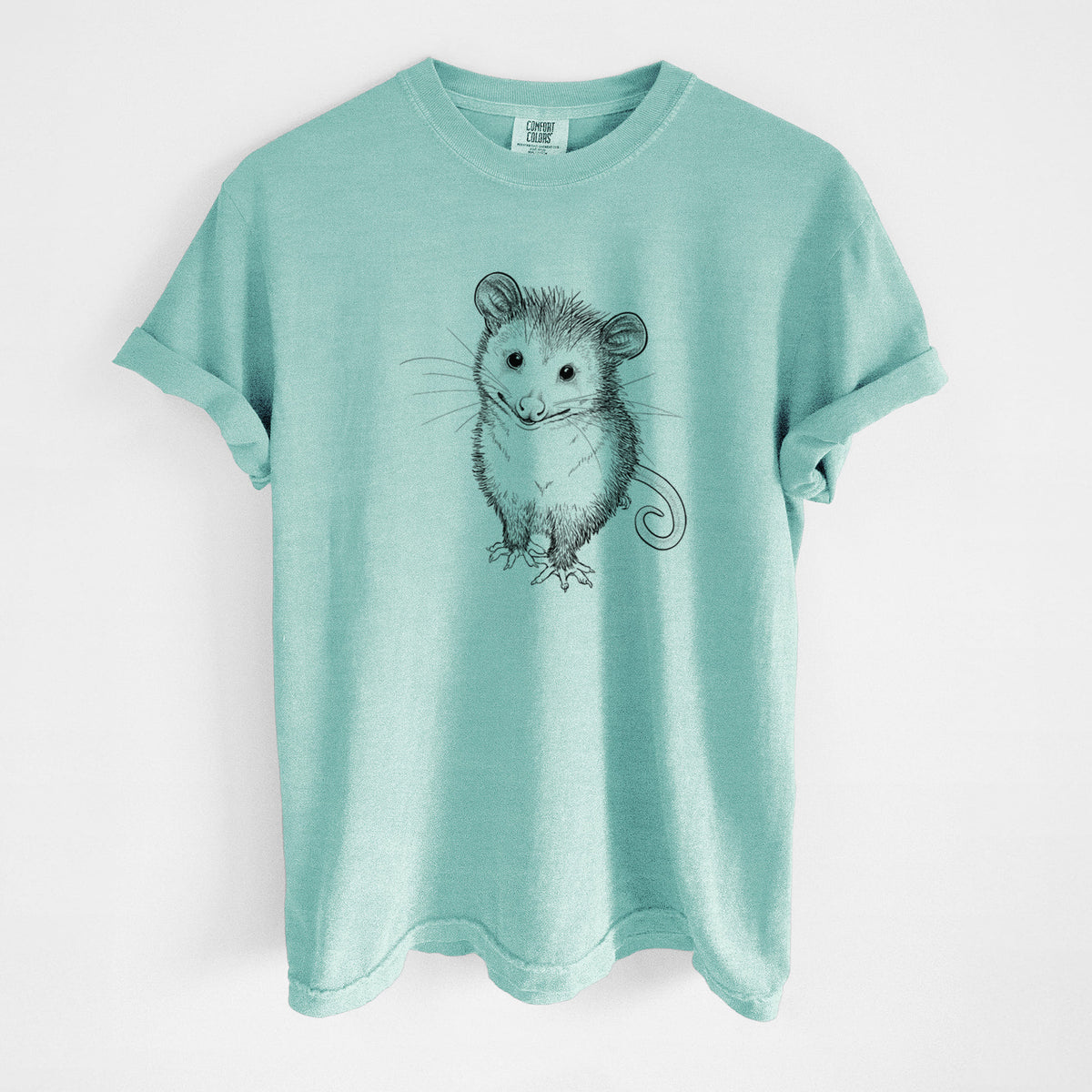 Chalky mint Comfort Colors t-shirt laid flat, printed with a black ink illustration of a wide-eyed baby opossum sitting.