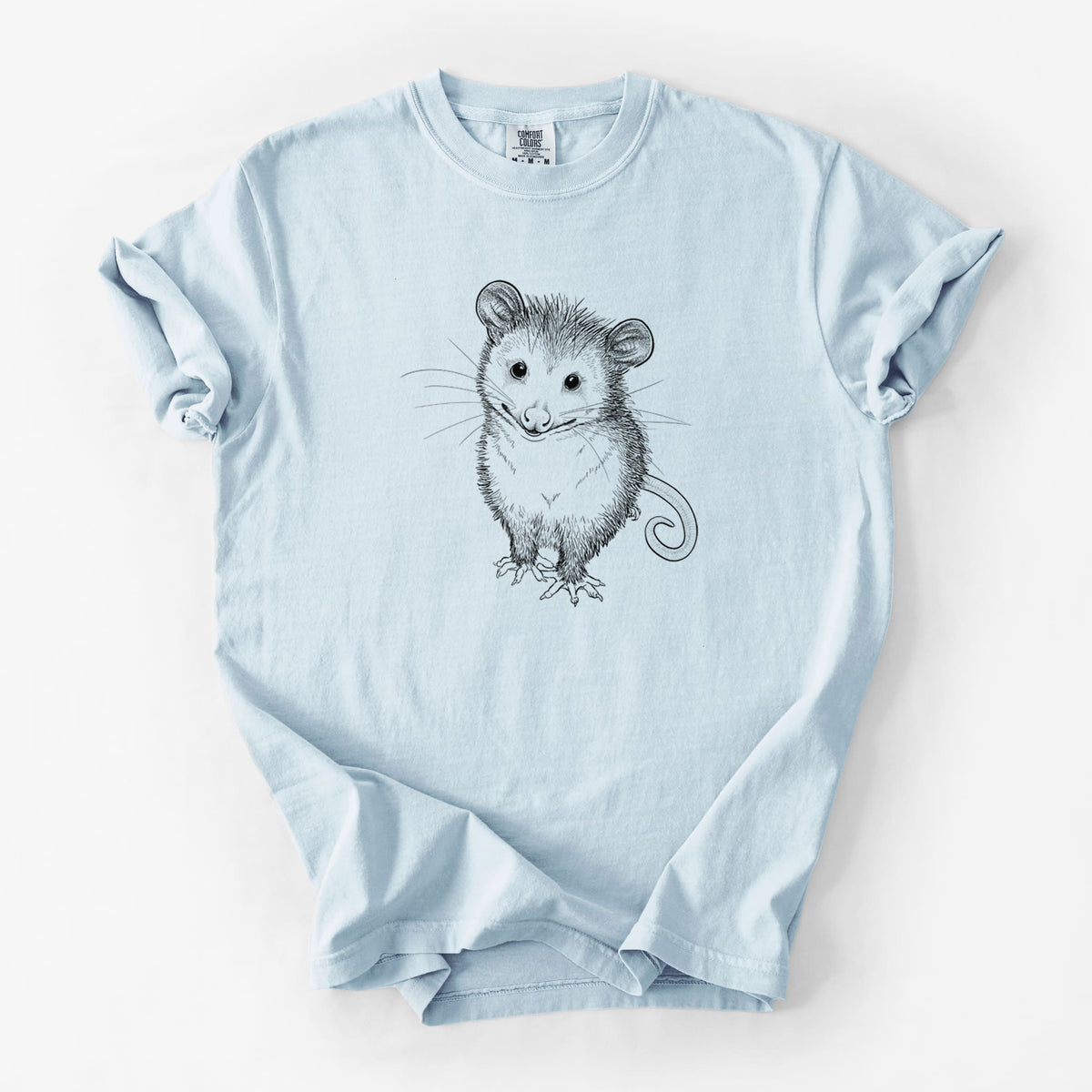 Chambray blue Comfort Colors t-shirt laid flat, printed with a black ink illustration of a wide-eyed baby opossum sitting.