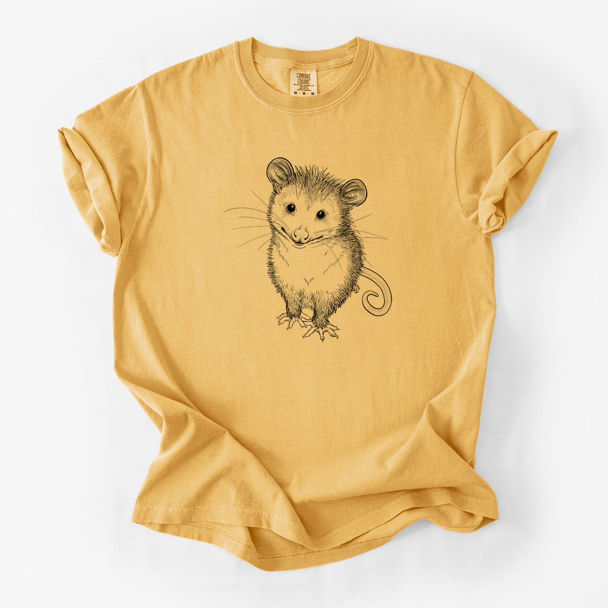 Golden wheat yellow Comfort Colors t-shirt laid flat, printed with a black ink illustration of a wide-eyed baby opossum sitting.