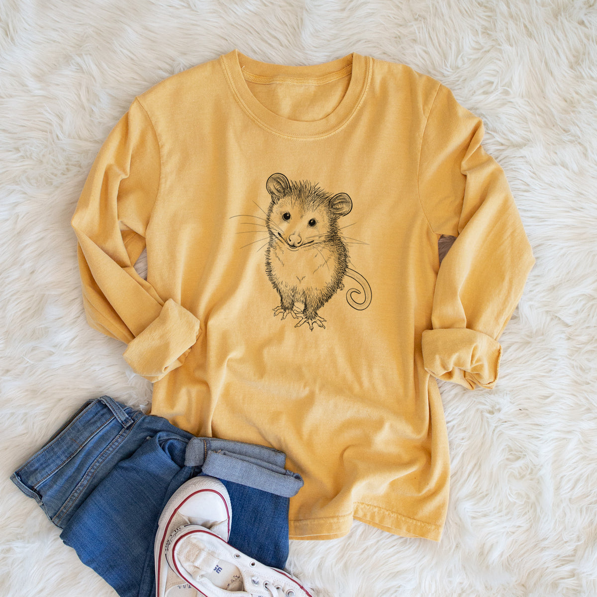 Golden wheat yellow Comfort Colors long sleeve shirt printed with a black ink illustration of a wide-eyed baby opossum sitting, shown in a lifestyle photo.