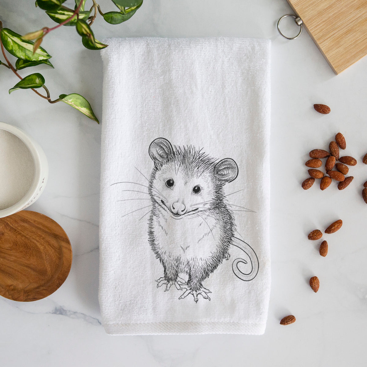 White hand towel printed with a black ink illustration of a wide-eyed baby opossum sitting.