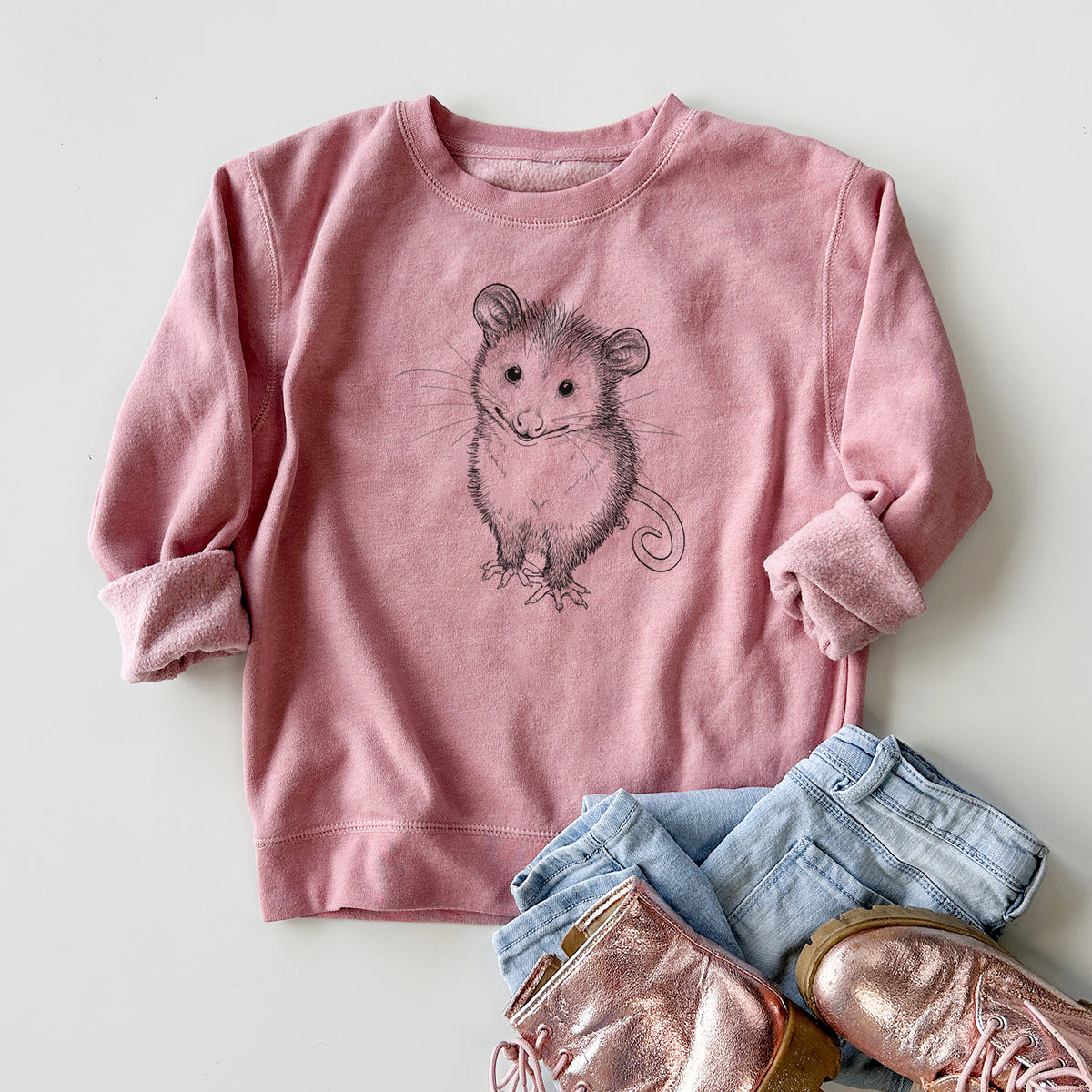Youth crewneck sweatshirt printed with a black ink illustration of a wide-eyed baby opossum sitting, styled flat with jeans and boots.