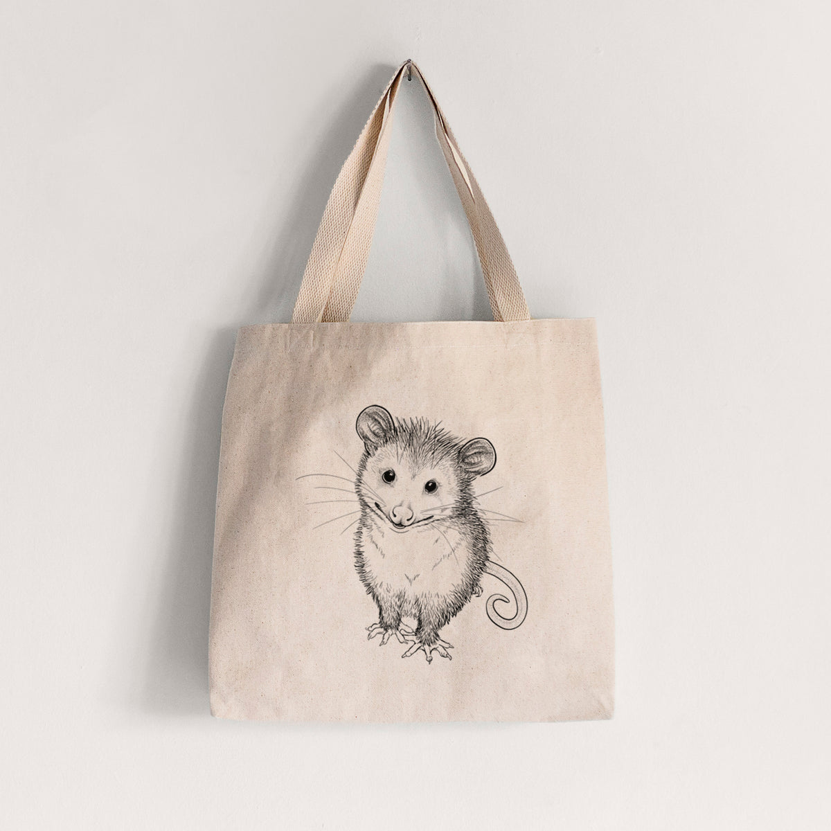 Natural canvas tote bag printed with a black ink illustration of a wide-eyed baby opossum sitting.
