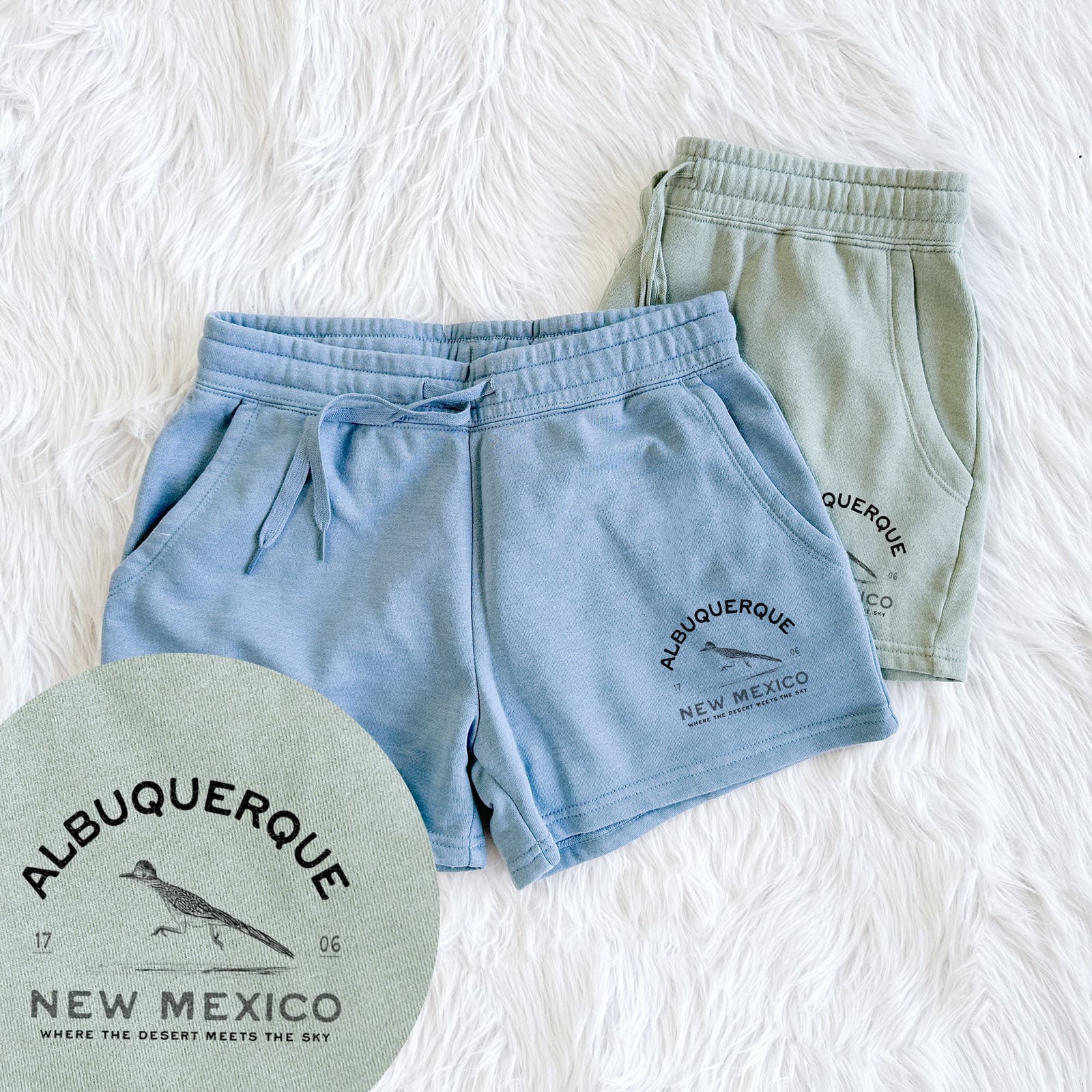 Two pairs of Cali Wave shorts in different colors printed with a black ink roadrunner with the words Albuquerque New Mexico, 1706, Where the Desert Meets the Sky, with a close-up of the print.