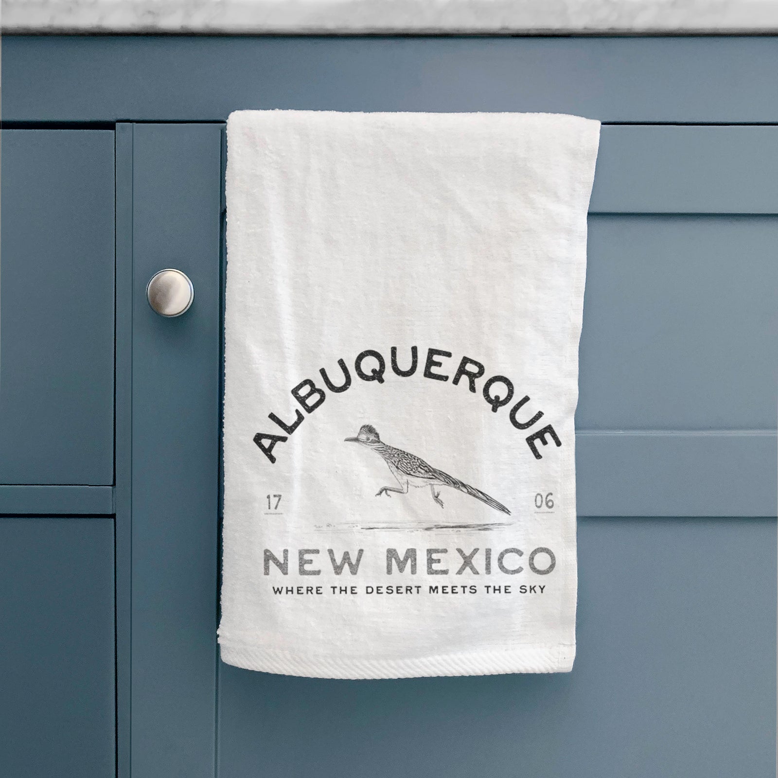 White hand towel printed with a black ink roadrunner with the words Albuquerque New Mexico, 1706, Where the Desert Meets the Sky.