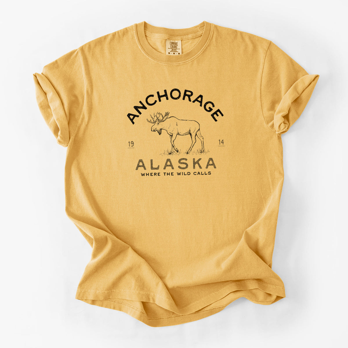 Golden wheat yellow Comfort Colors t-shirt laid flat, printed with a black ink moose with the words Anchorage Alaska, 1914, Where the Wild Calls.