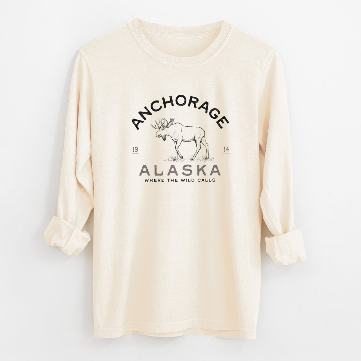 Ivory Comfort Colors long sleeve shirt laid flat with the cuffs rolled, printed with a black ink moose with the words Anchorage Alaska, 1914, Where the Wild Calls.