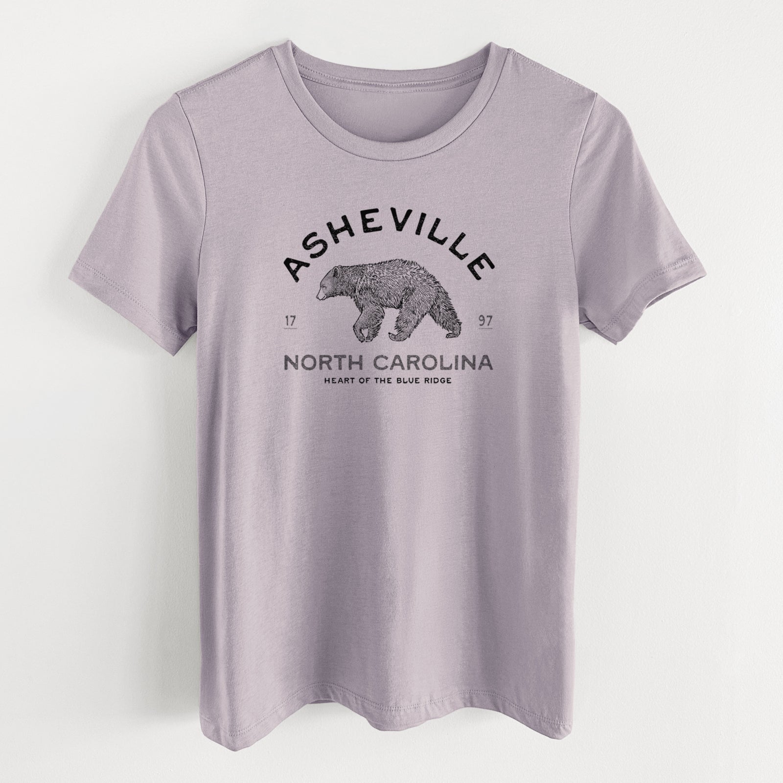 Light violet women's relaxed fit cotton t-shirt laid flat, printed with a black ink bear with the words Asheville North Carolina, Heart of the Blue Ridge.