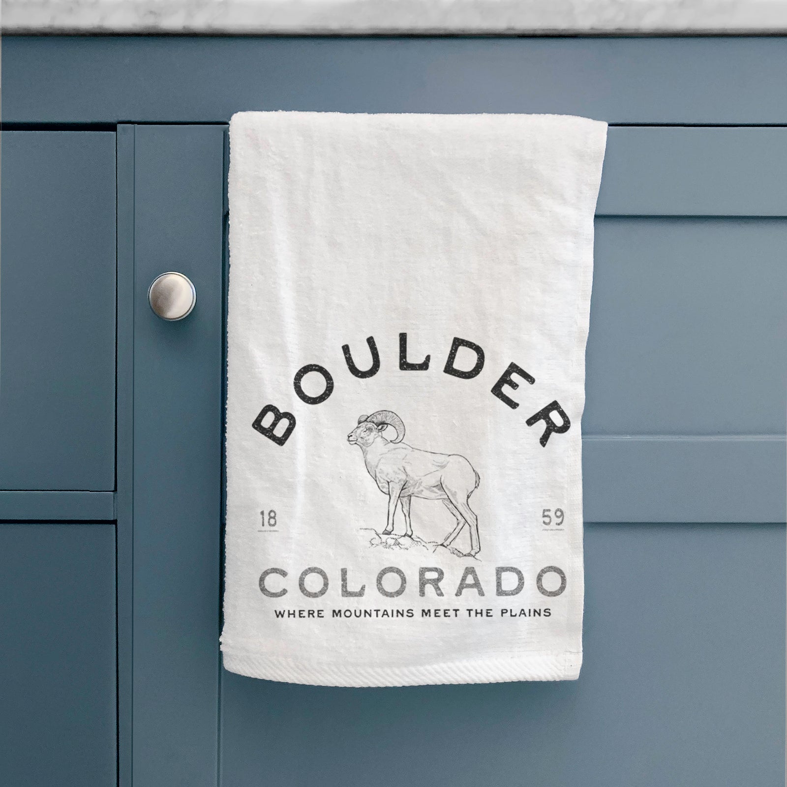 White hand towel printed with a black ink bighorn sheep with the words Boulder Colorado, Where Mountains Meet the Plains, 1859.
