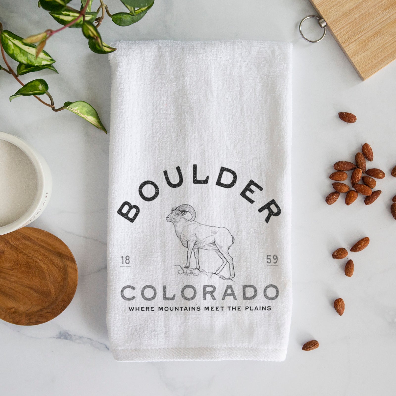 White hand towel printed with a black ink bighorn sheep with the words Boulder Colorado, Where Mountains Meet the Plains, 1859.
