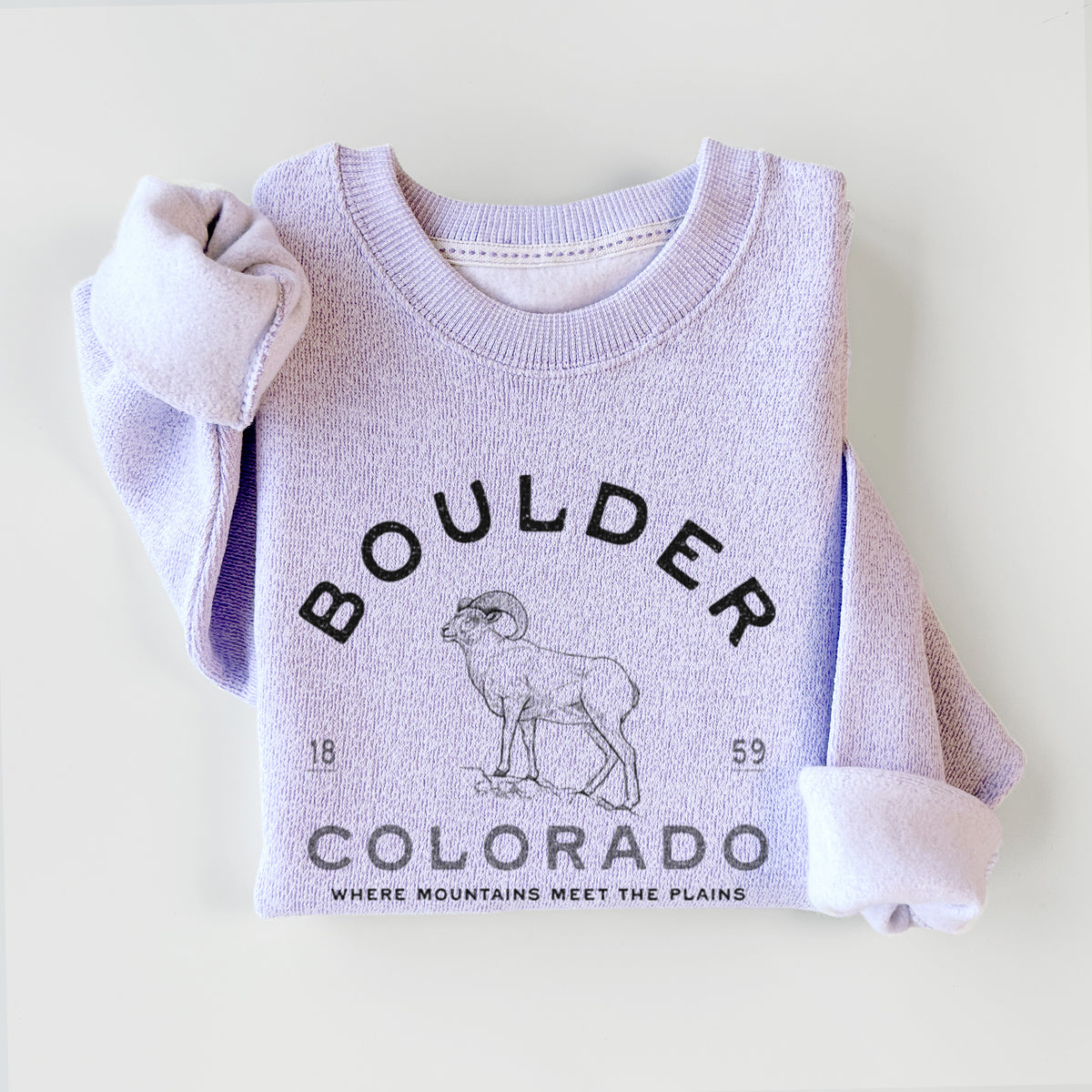 Ice purple knit sweatshirt printed with a black ink bighorn sheep with the words Boulder Colorado, Where Mountains Meet the Plains, 1859, styled flat.