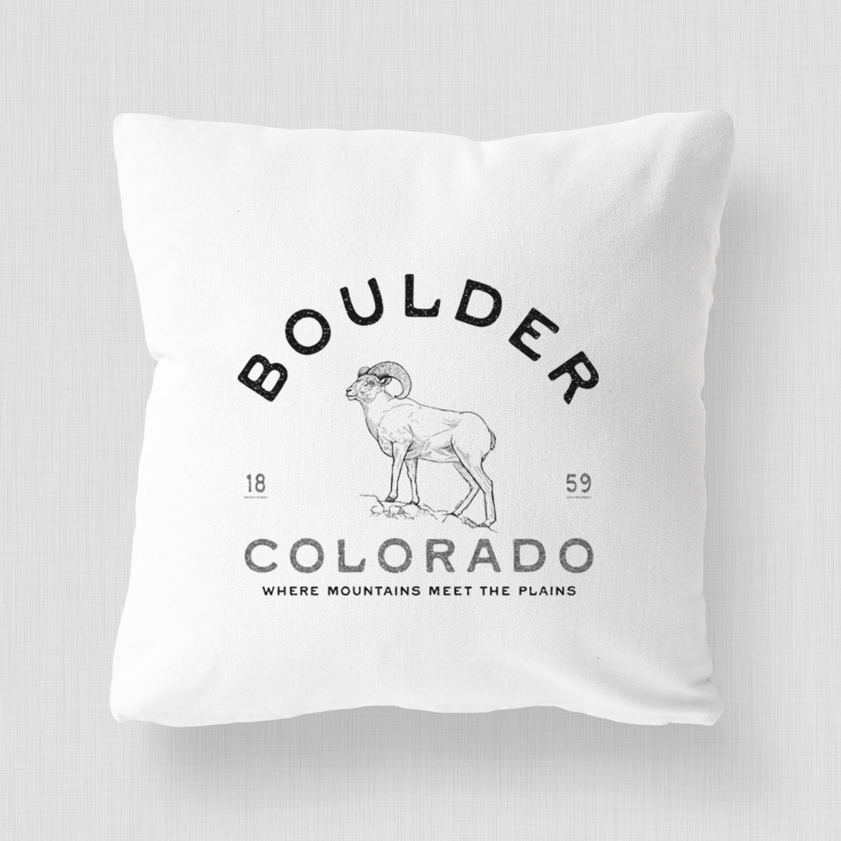 White pillow cover printed with a black ink bighorn sheep with the words Boulder Colorado, Where Mountains Meet the Plains, 1859.
