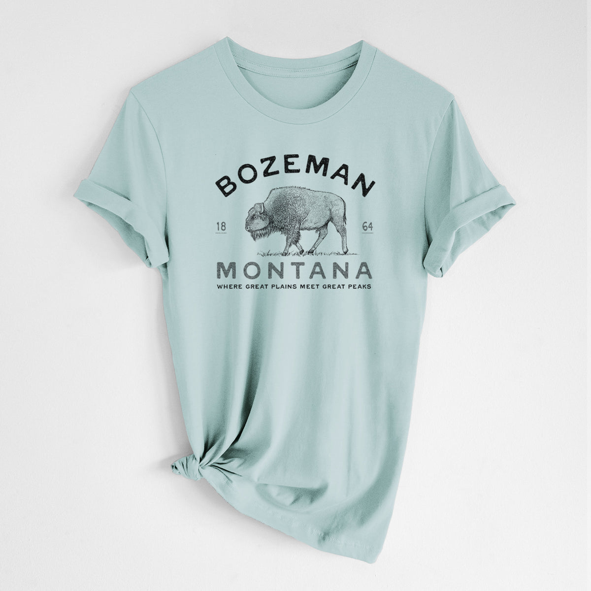 Dusty blue lightweight cotton t-shirt laid flat with the sleeves rolled, printed with a black ink bison with the words Bozeman Montana, 1864, Where Great Plains Meet Great Peaks.