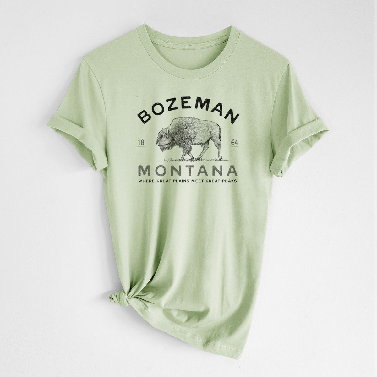 Spring green lightweight cotton t-shirt laid flat with the sleeves rolled, printed with a black ink bison with the words Bozeman Montana, 1864, Where Great Plains Meet Great Peaks.