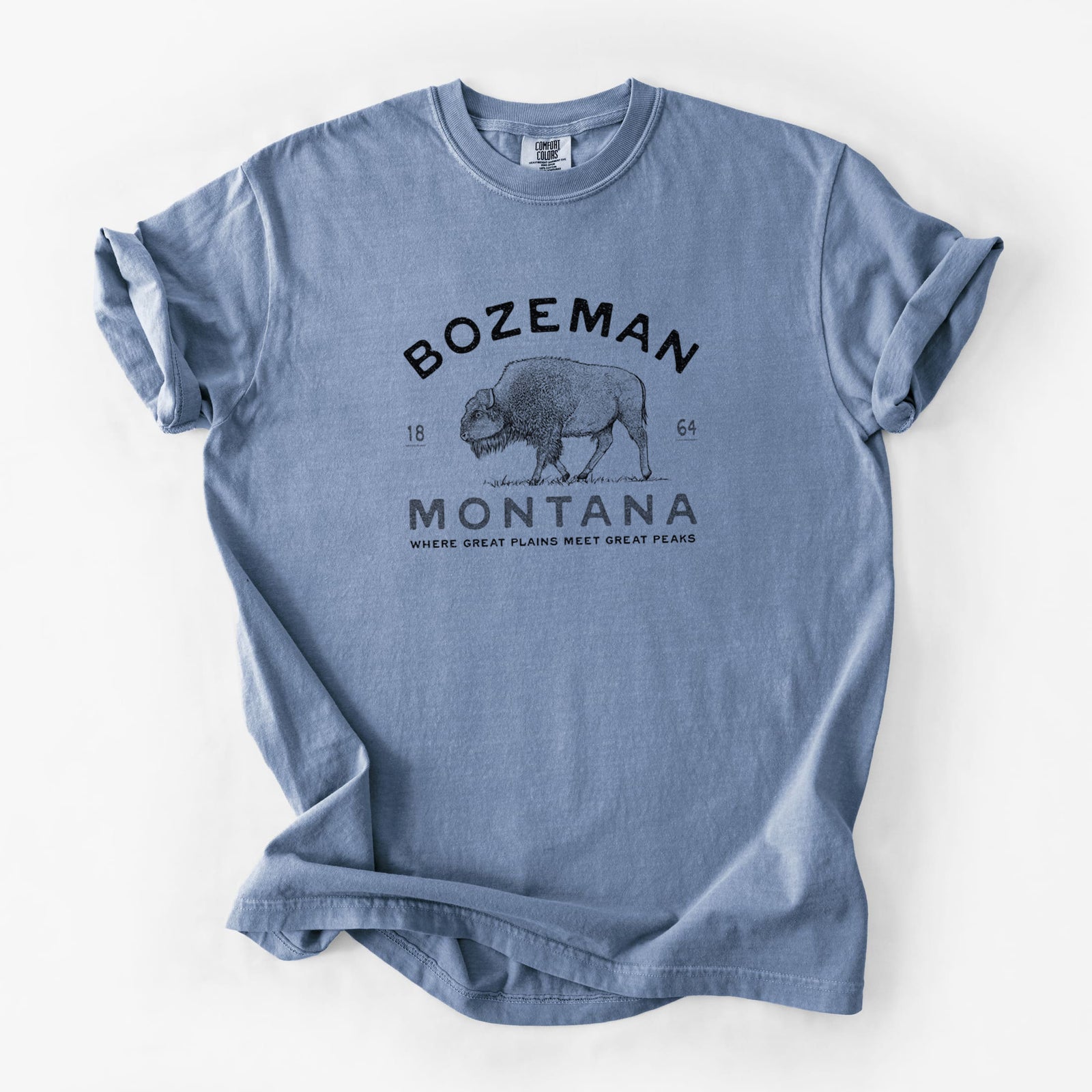 Blue jean Comfort Colors t-shirt laid flat, printed with a black ink bison with the words Bozeman Montana, 1864, Where Great Plains Meet Great Peaks.