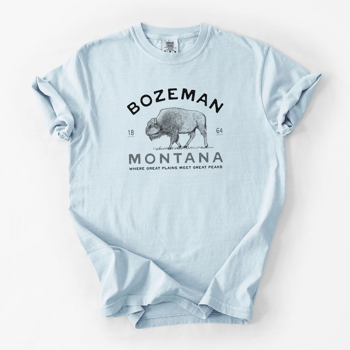 Chambray blue Comfort Colors t-shirt laid flat, printed with a black ink bison with the words Bozeman Montana, 1864, Where Great Plains Meet Great Peaks.