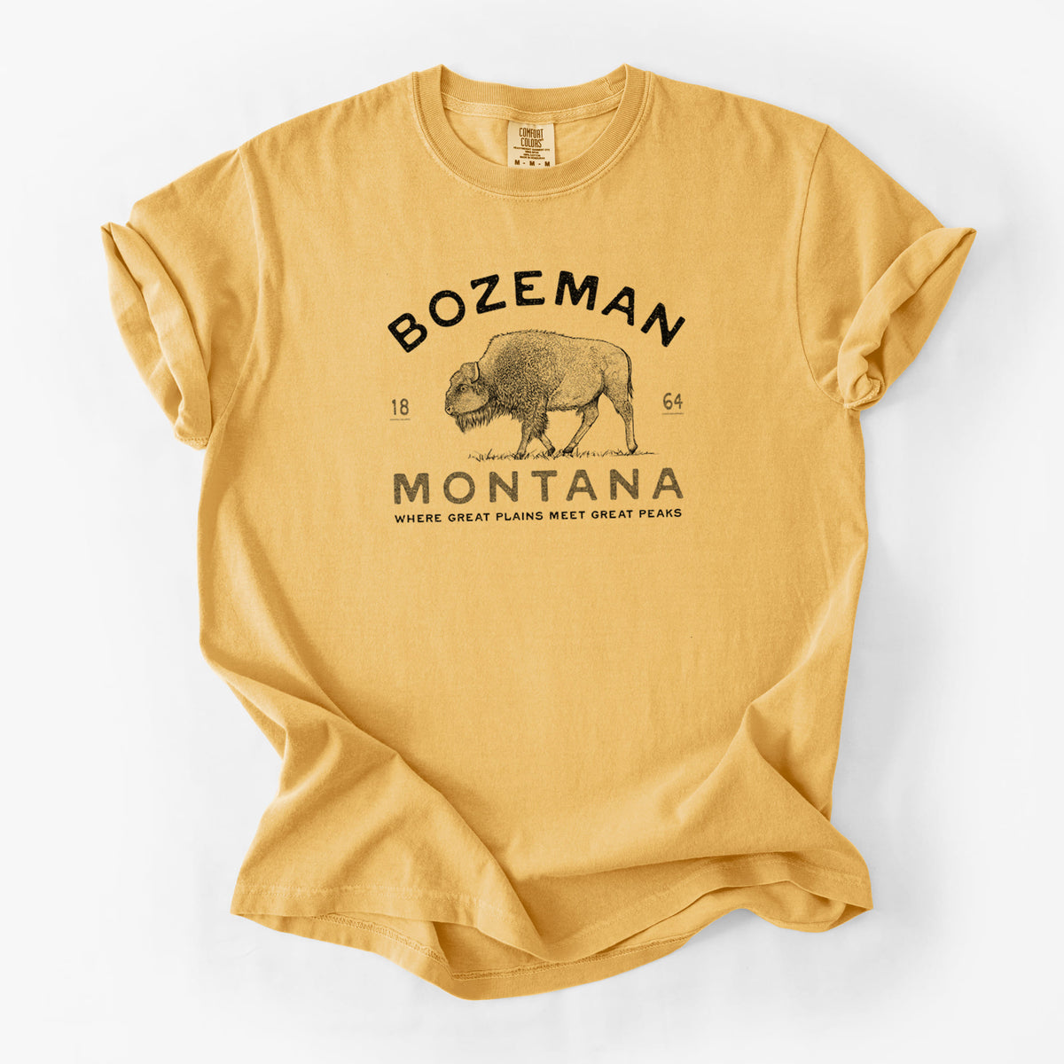 Golden wheat yellow Comfort Colors t-shirt laid flat, printed with a black ink bison with the words Bozeman Montana, 1864, Where Great Plains Meet Great Peaks.
