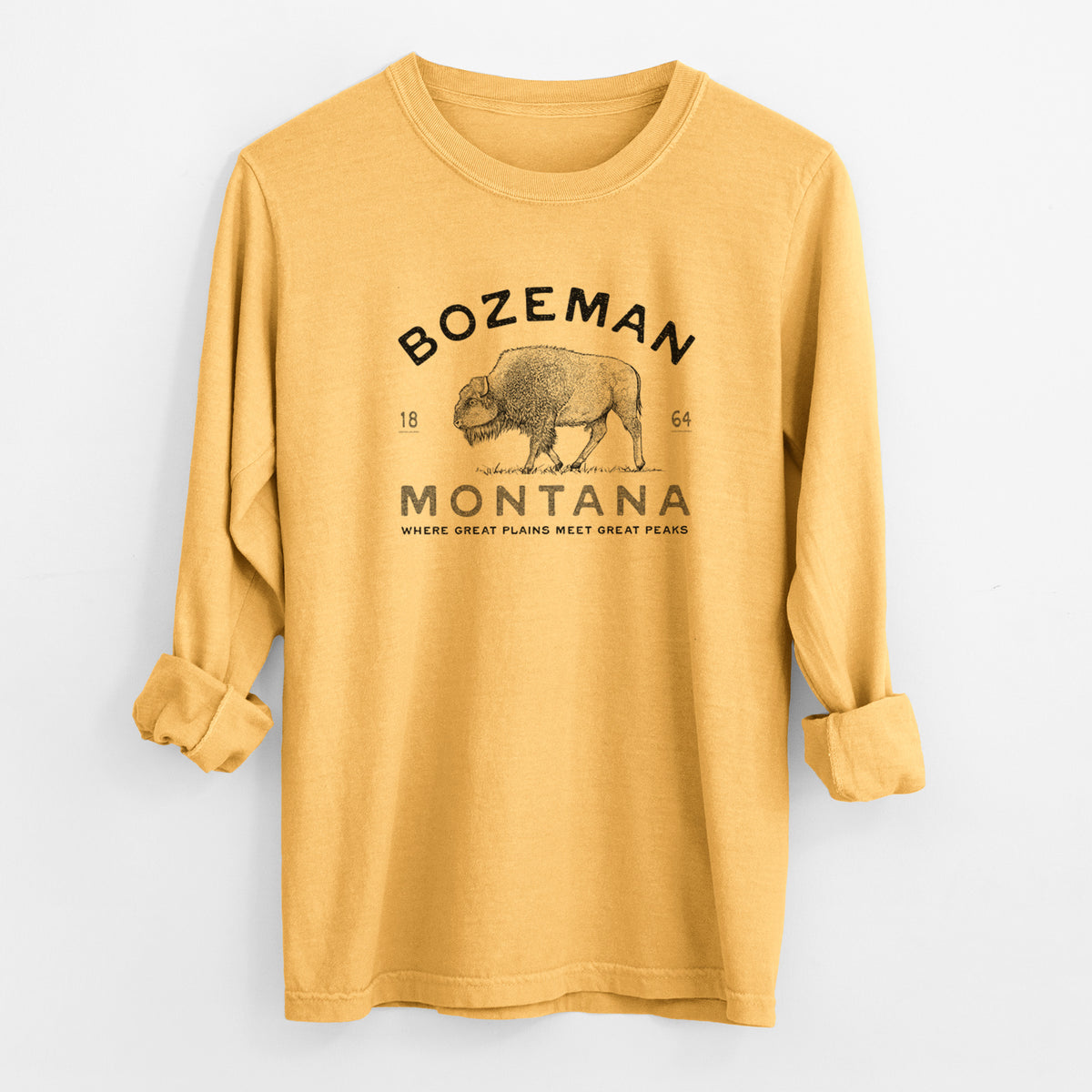 Golden wheat yellow Comfort Colors long sleeve shirt laid flat with the cuffs rolled, printed with a black ink bison with the words Bozeman Montana, 1864, Where Great Plains Meet Great Peaks.