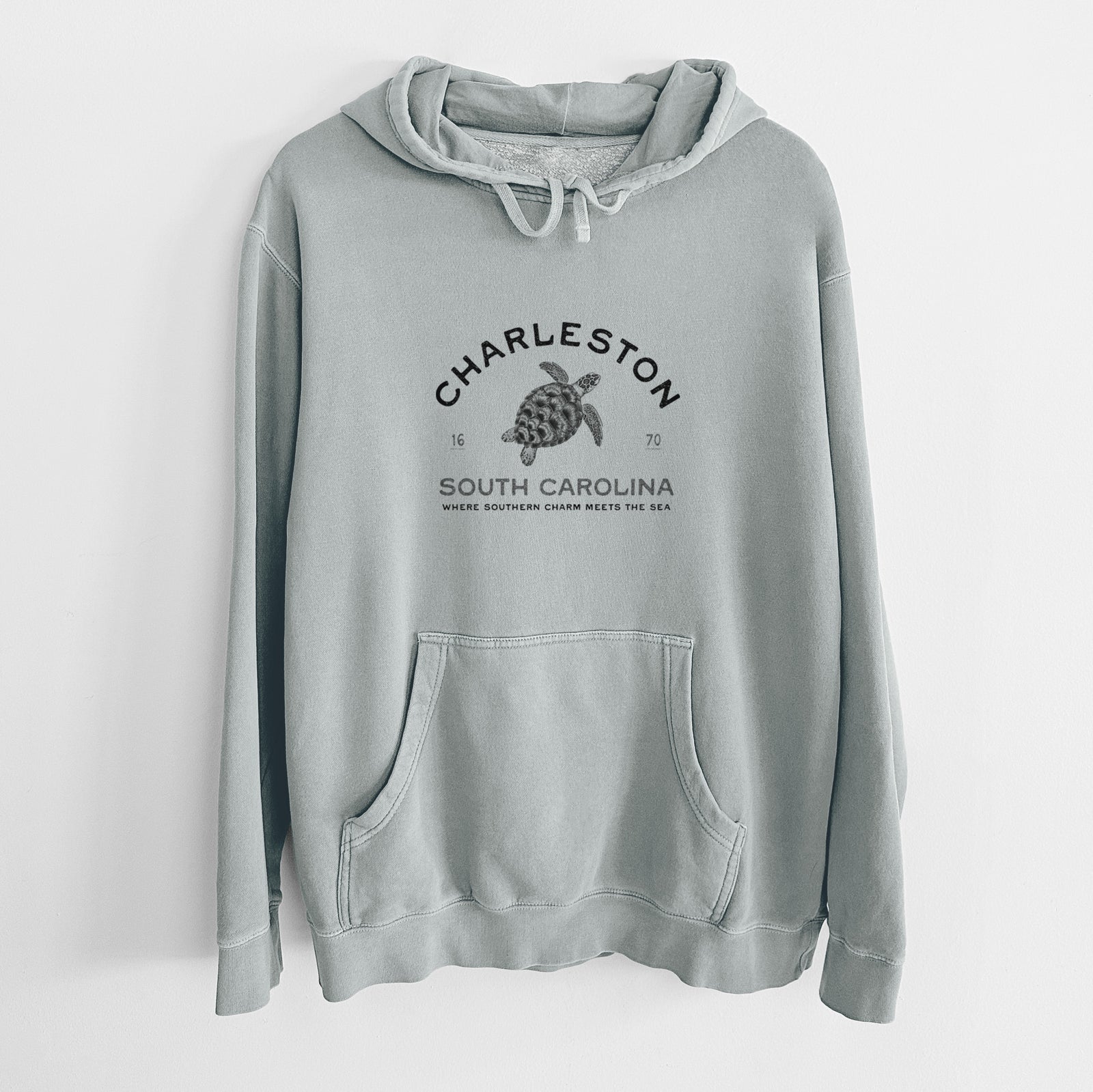 Sage green pigment dyed hoodie laid flat, printed with a black ink sea turtle with the words Charleston South Carolina, Where Southern Charm Meets the Sea.