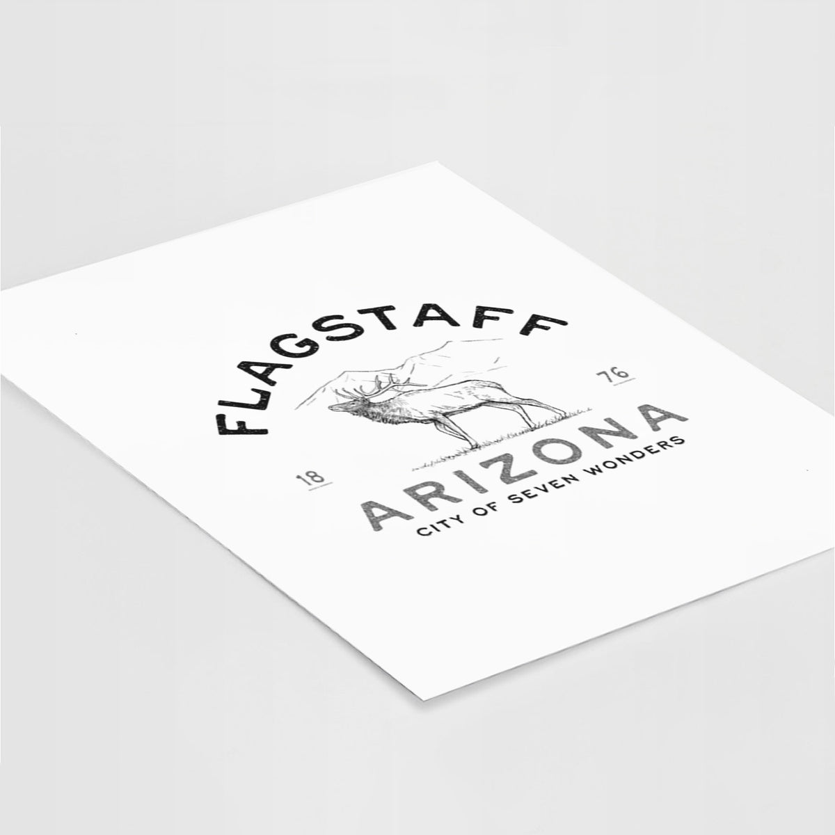 Art print of a black ink elk with the words Flagstaff Arizona, City of Seven Wonders, lying at an angle on a white surface.