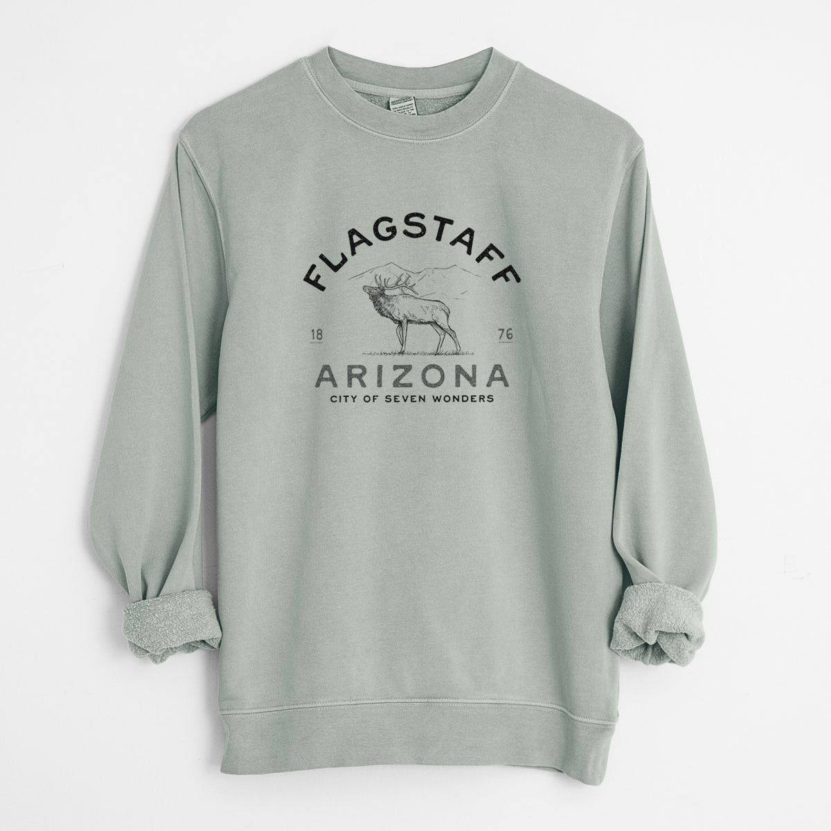 Sage green pigment dyed crewneck sweatshirt laid flat with the sleeves rolled, printed with a black ink elk with the words Flagstaff Arizona, City of Seven Wonders.