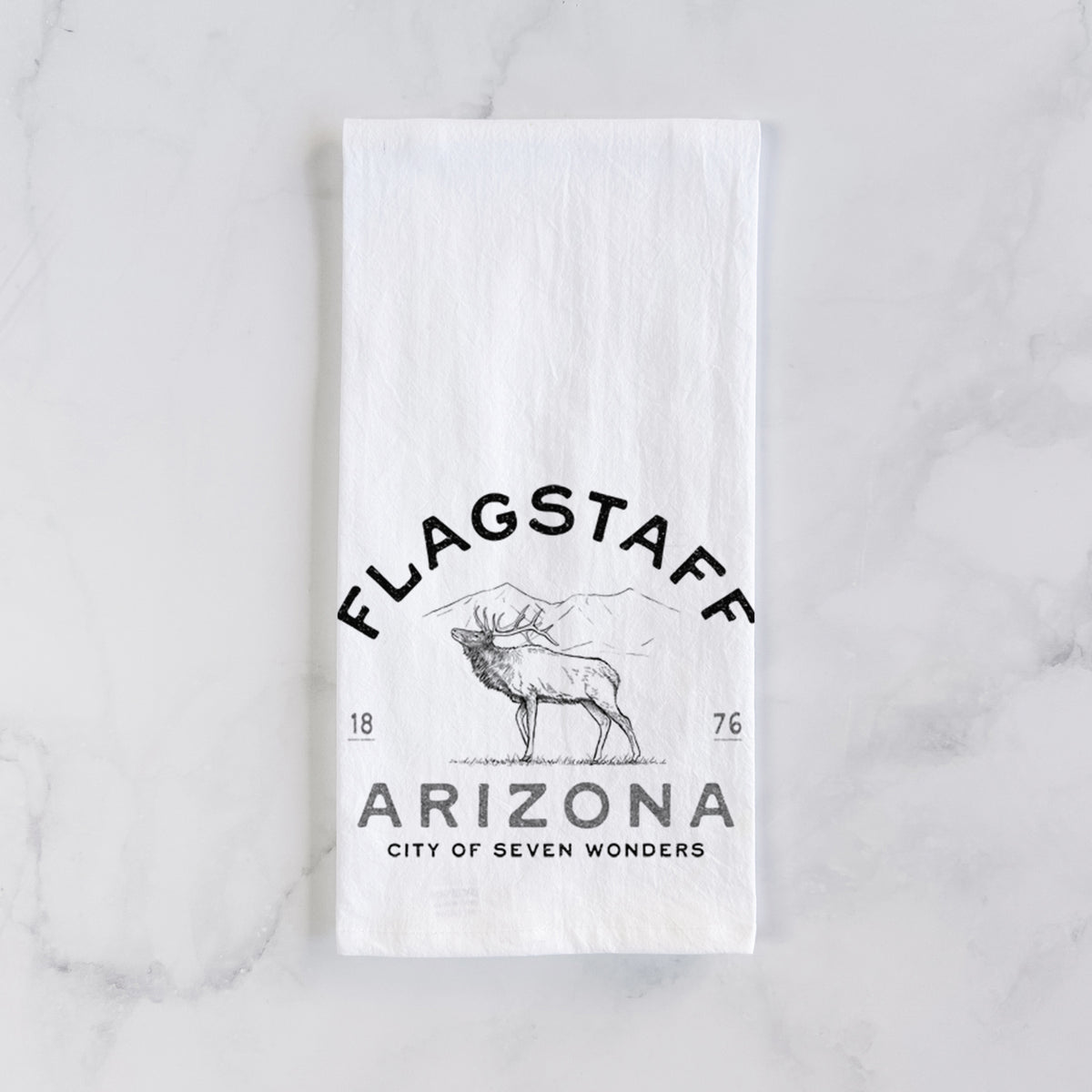 White cotton tea towel laid flat on marble, printed with a black ink elk with the words Flagstaff Arizona, City of Seven Wonders.