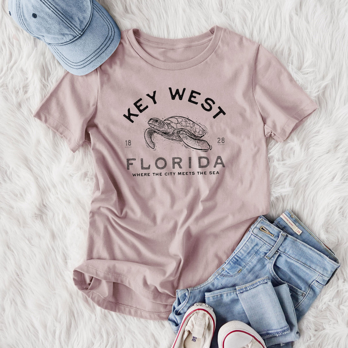 Women's relaxed fit cotton t-shirt printed with a black ink sea turtle with the words Key West Florida, styled flat on a white faux fur rug with jeans.