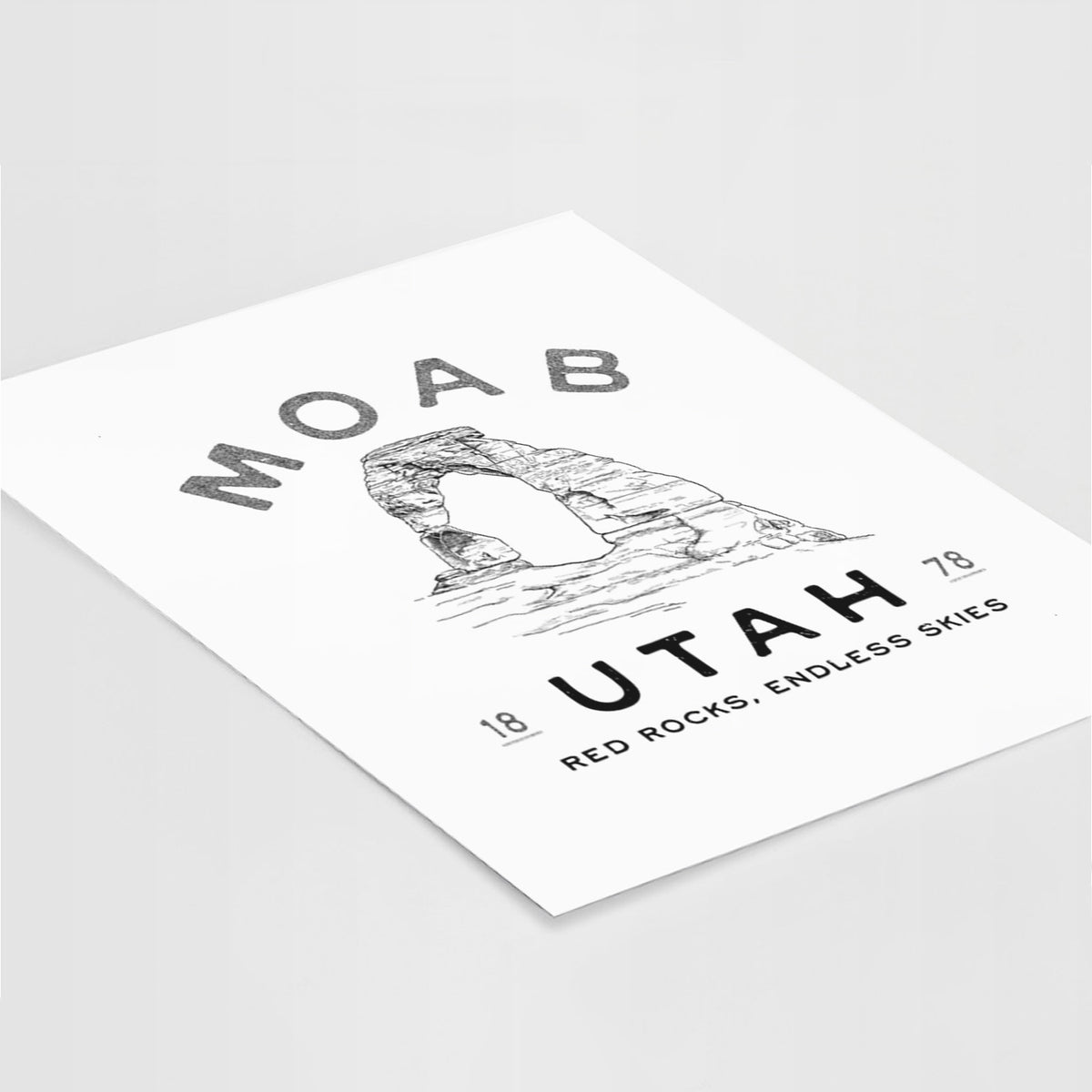 Art print of a black ink illustration of Delicate Arch with the words Moab Utah, 1878, lying at an angle on a white surface.
