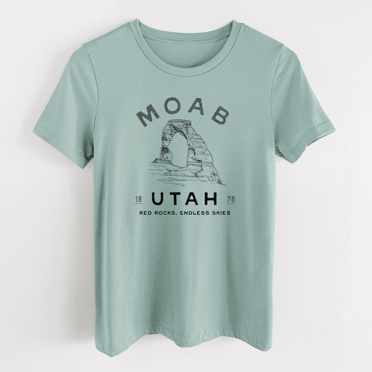 Dusty blue women's relaxed fit cotton t-shirt laid flat, printed with a black ink illustration of Delicate Arch with the words Moab Utah, 1878.