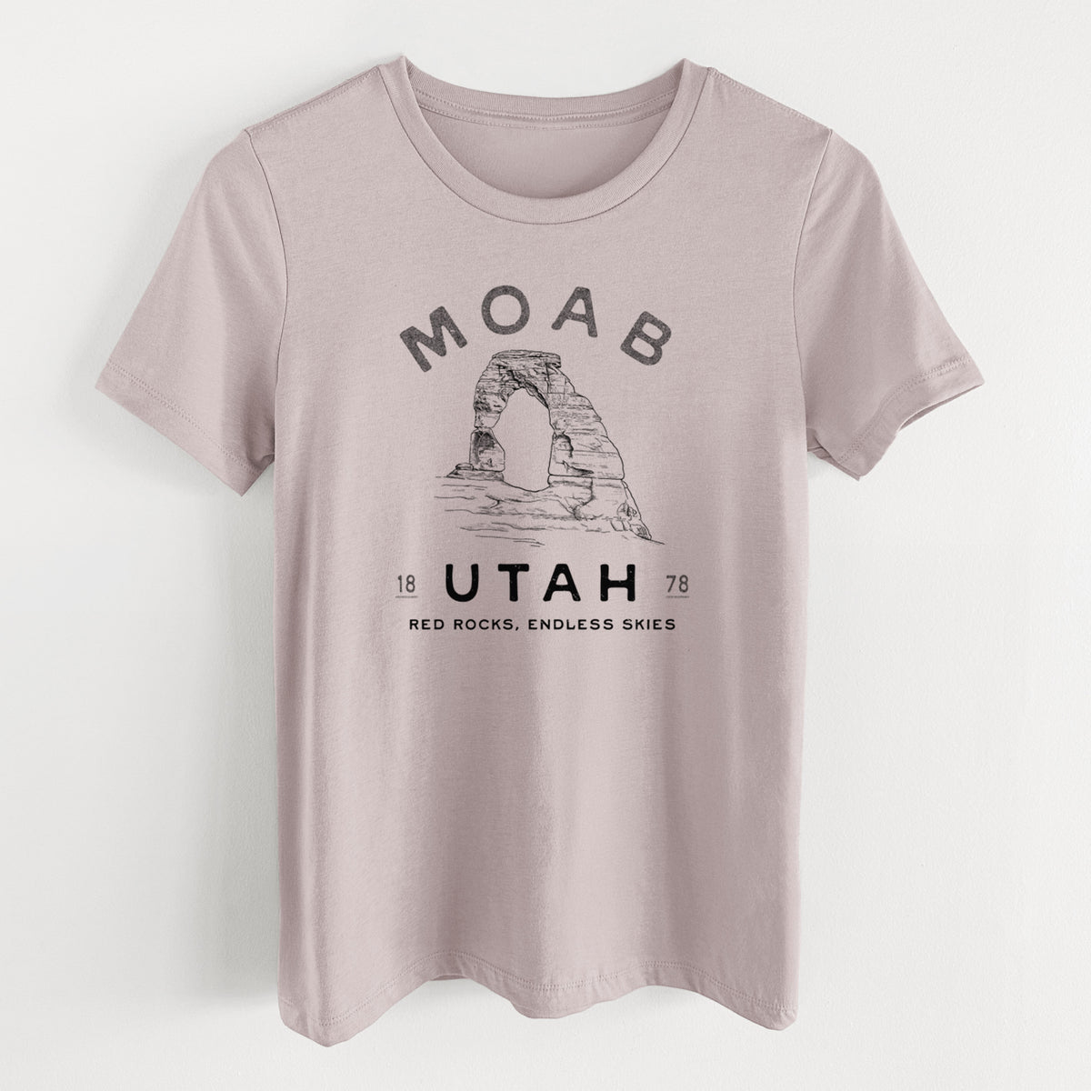 Pink gravel women's relaxed fit cotton t-shirt laid flat, printed with a black ink illustration of Delicate Arch with the words Moab Utah, 1878.