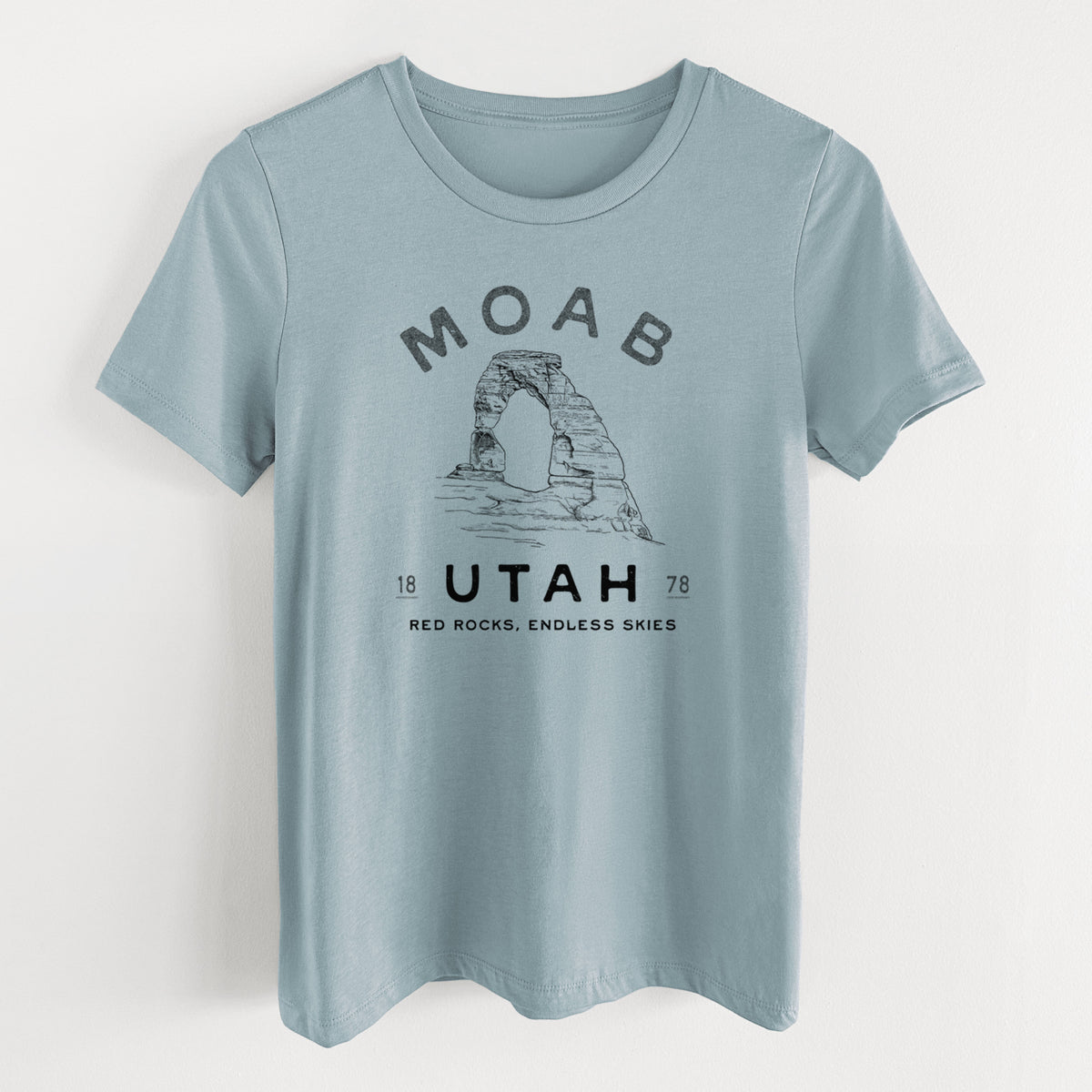 Vintage denim women's relaxed fit cotton t-shirt laid flat, printed with a black ink illustration of Delicate Arch with the words Moab Utah, 1878.