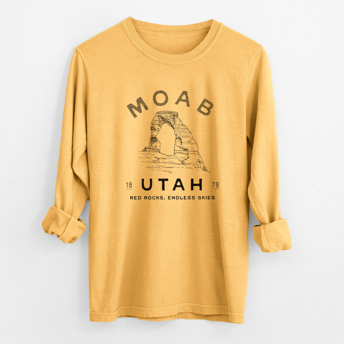 Golden wheat yellow Comfort Colors long sleeve shirt laid flat with the cuffs rolled, printed with a black ink illustration of Delicate Arch with the words Moab Utah, 1878.