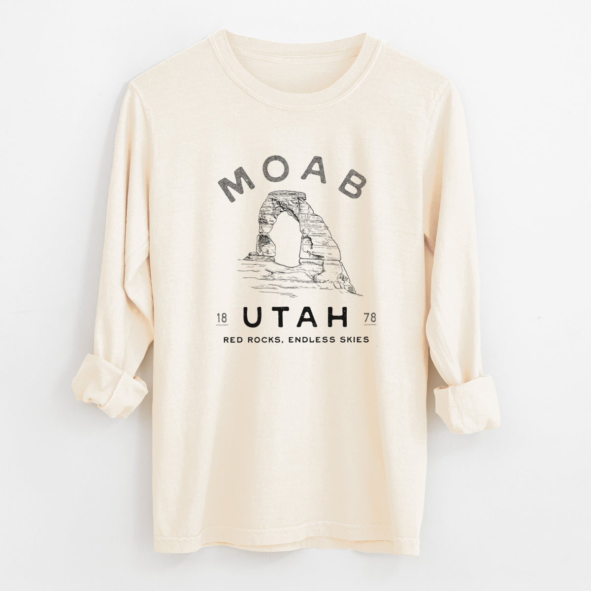 Ivory Comfort Colors long sleeve shirt laid flat with the cuffs rolled, printed with a black ink illustration of Delicate Arch with the words Moab Utah, 1878.