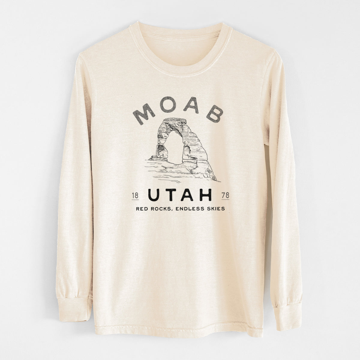 Ivory Comfort Colors long sleeve shirt laid flat, printed with a black ink illustration of Delicate Arch with the words Moab Utah, 1878.
