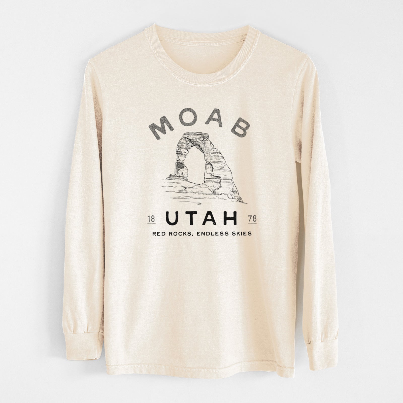 Ivory Comfort Colors long sleeve shirt laid flat, printed with a black ink illustration of Delicate Arch with the words Moab Utah, 1878.