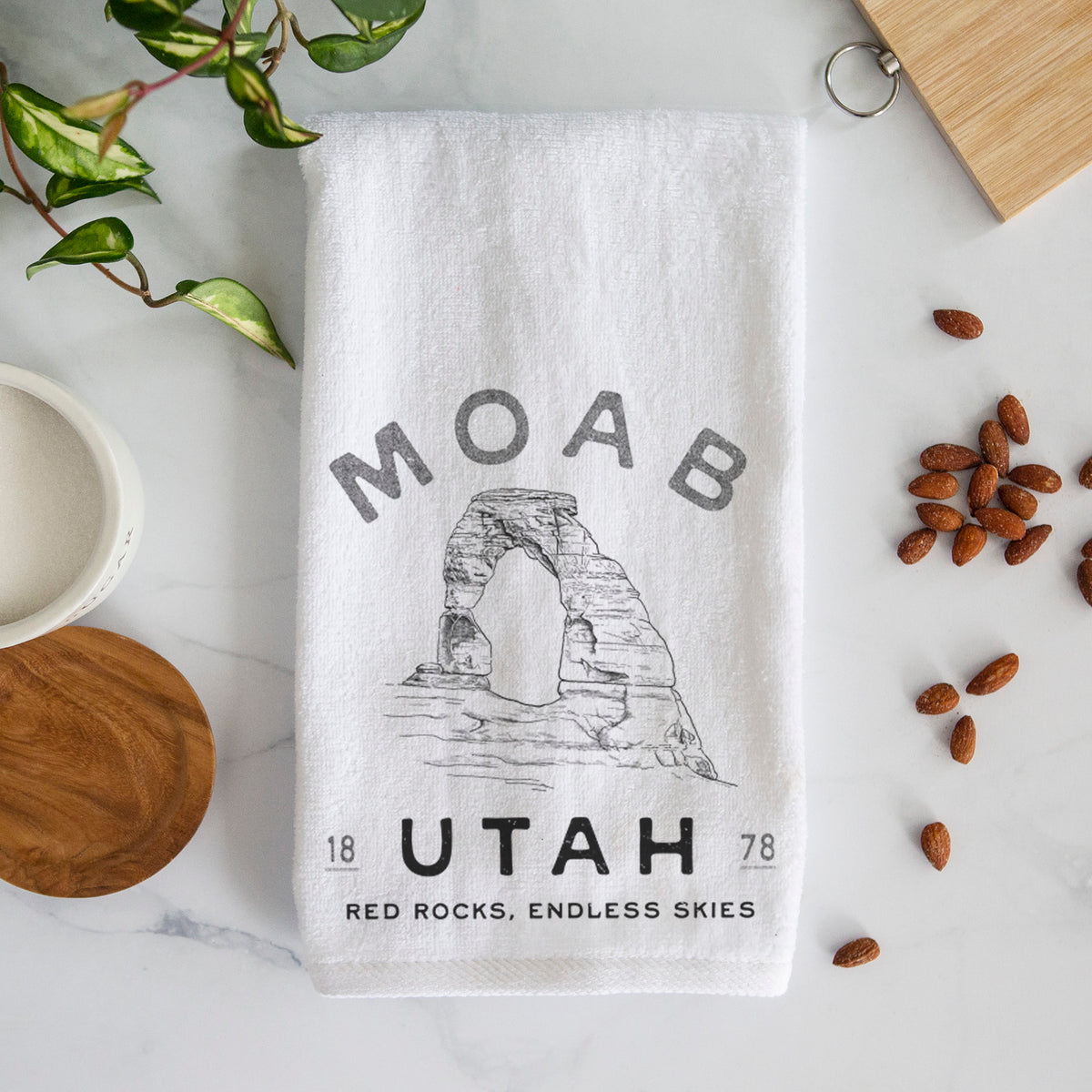 White hand towel printed with a black ink illustration of Delicate Arch with the words Moab Utah, 1878.