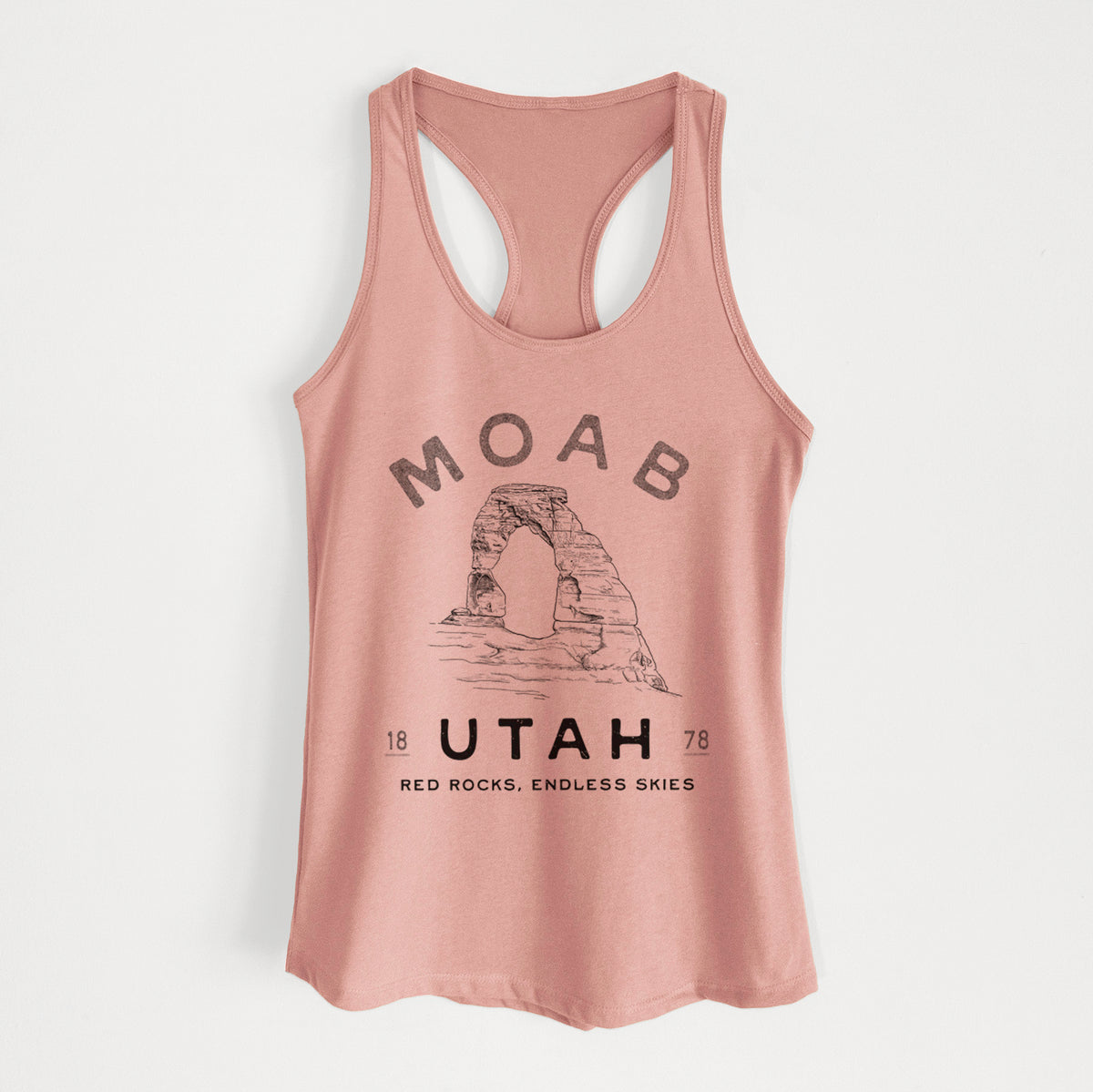 Desert pink women's racerback tank top laid flat, printed with a black ink illustration of Delicate Arch with the words Moab Utah, 1878.