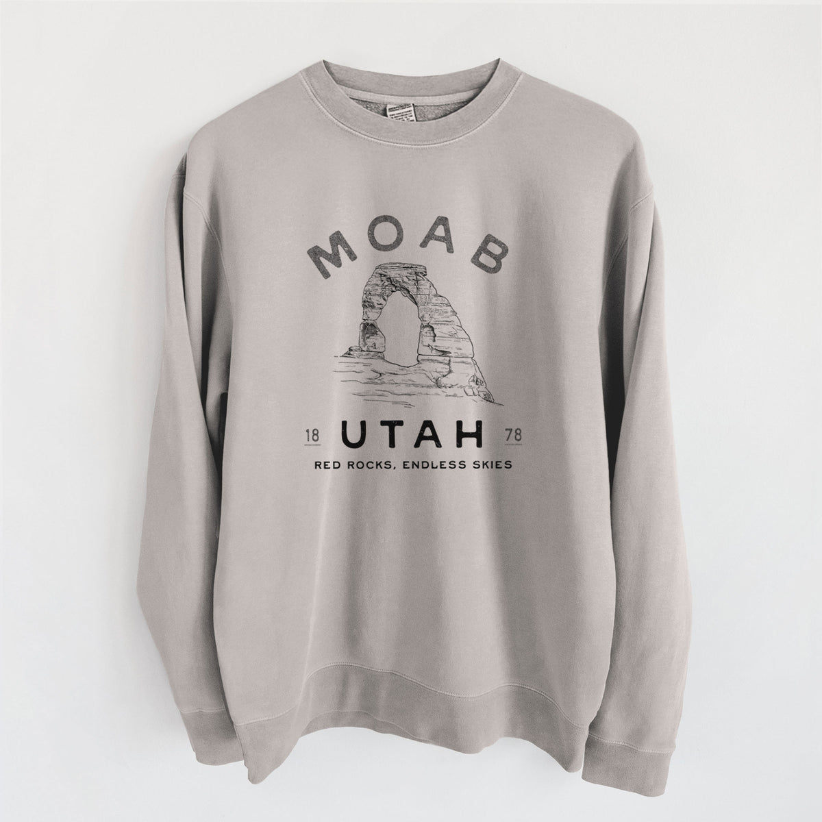 Cement grey pigment dyed crewneck sweatshirt laid flat, printed with a black ink illustration of Delicate Arch with the words Moab Utah, 1878.