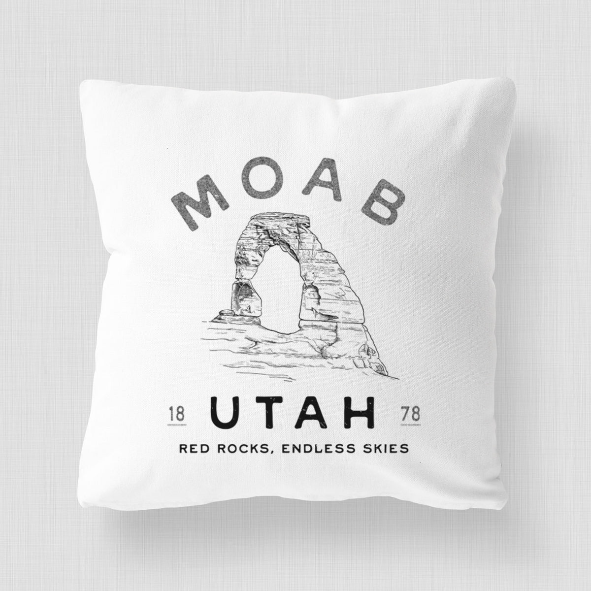 White pillow cover printed with a black ink illustration of Delicate Arch with the words Moab Utah, 1878.