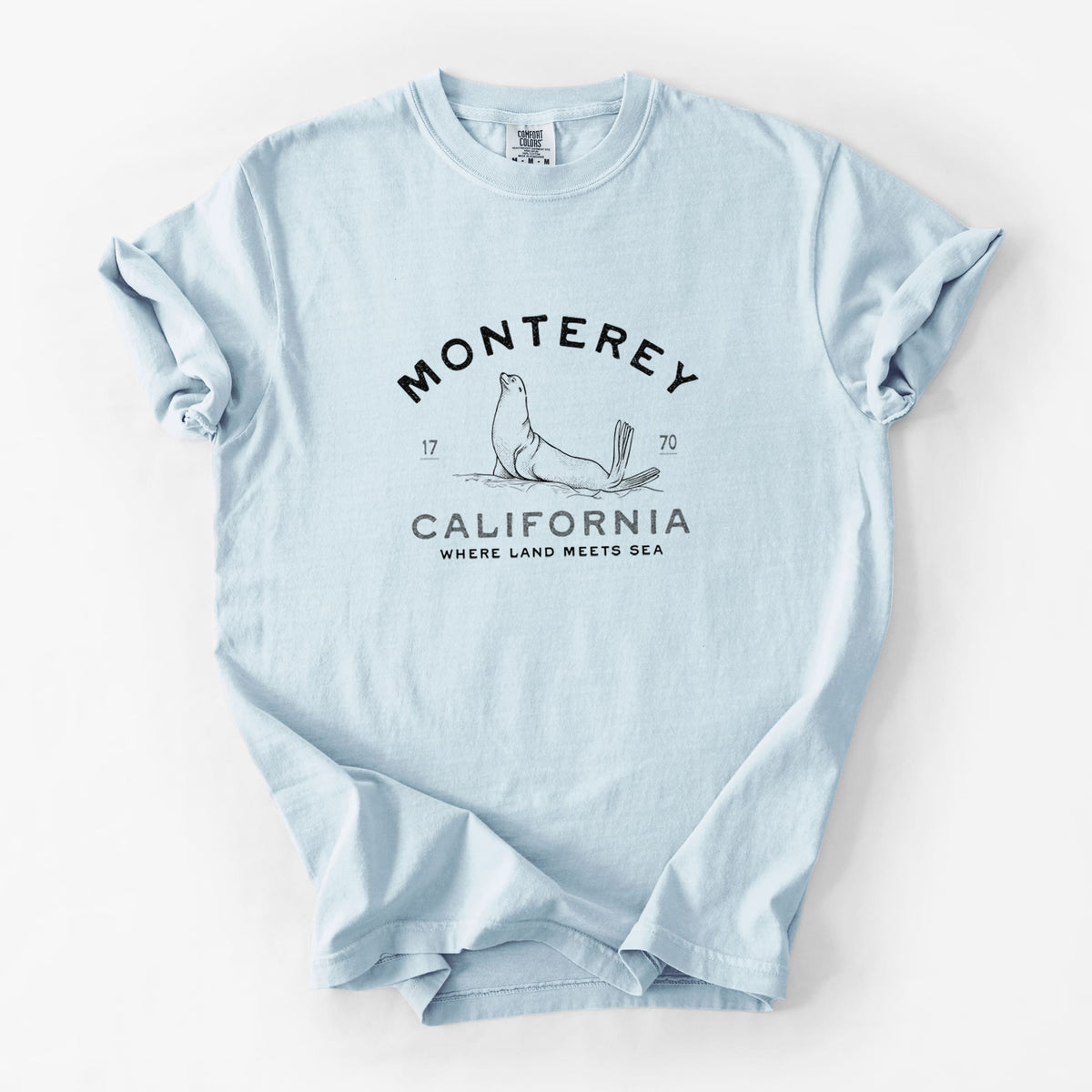 Chambray blue Comfort Colors t-shirt laid flat, printed with a black ink sea lion with the words Monterey California, 1770, Where Land Meets Sea.