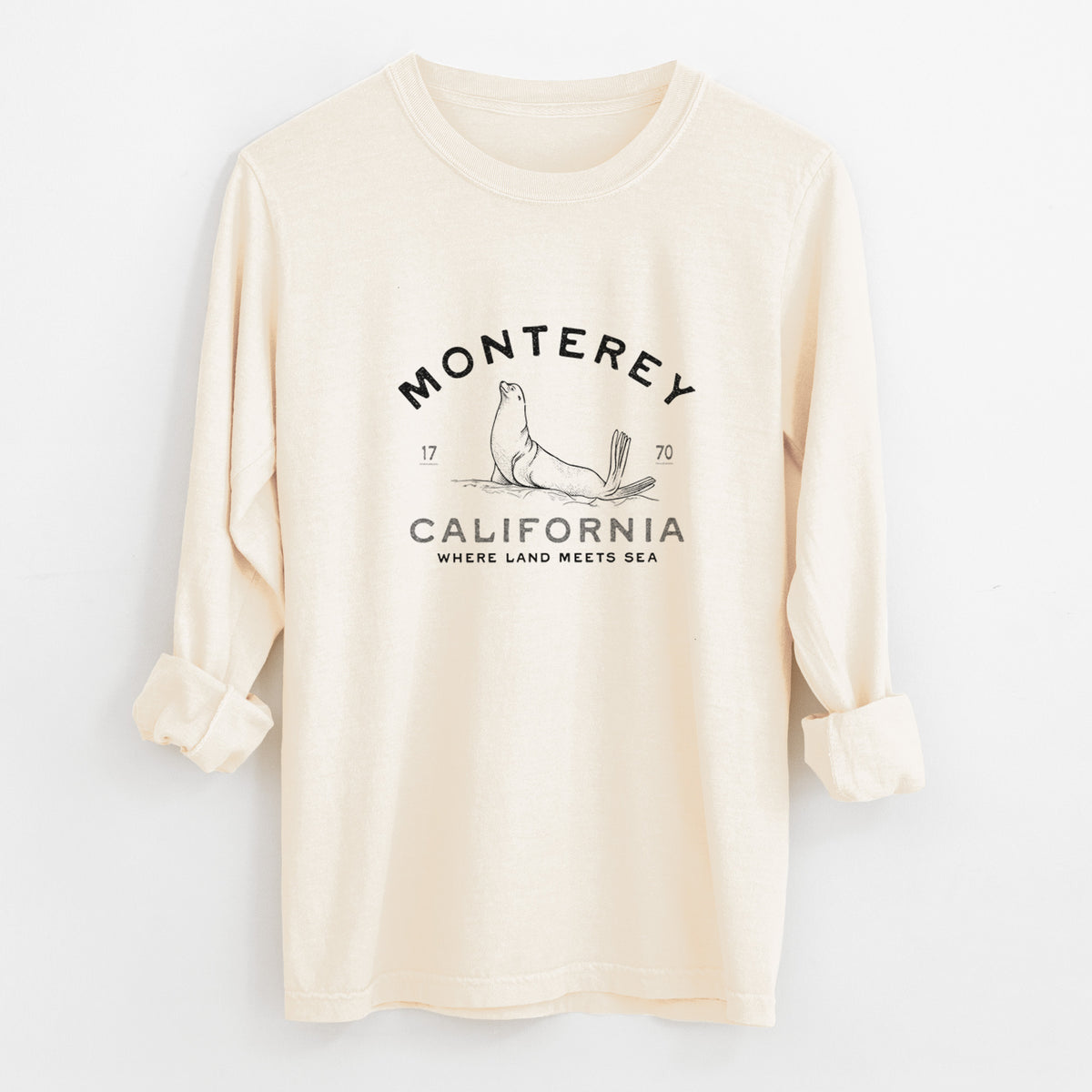 Ivory Comfort Colors long sleeve shirt laid flat with the cuffs rolled, printed with a black ink sea lion with the words Monterey California, 1770, Where Land Meets Sea.