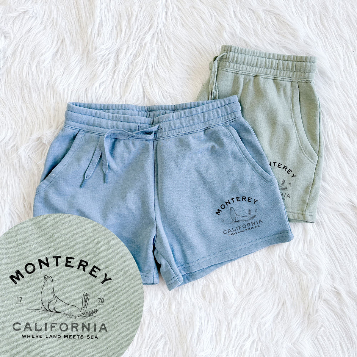 Two pairs of Cali Wave shorts in different colors printed with a black ink sea lion with the words Monterey California, 1770, Where Land Meets Sea, with a close-up of the print.