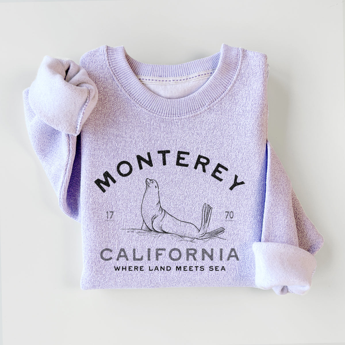 Ice purple knit sweatshirt printed with a black ink sea lion with the words Monterey California, 1770, Where Land Meets Sea, styled flat.