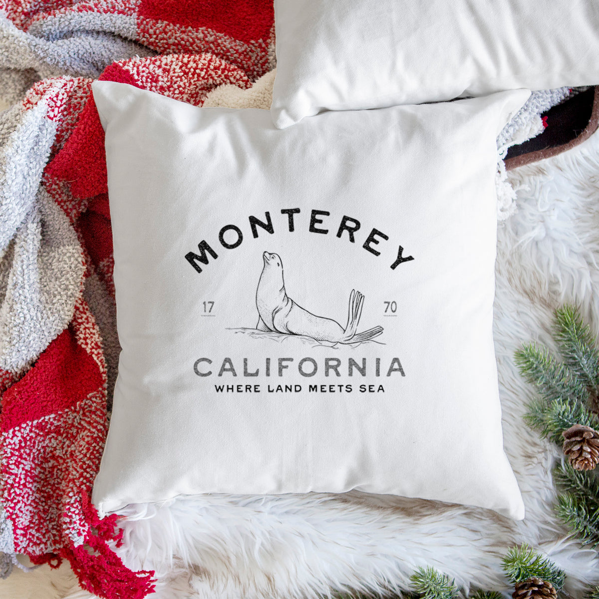 White pillow cover printed with a black ink sea lion with the words Monterey California, 1770, Where Land Meets Sea, on a woven chair.