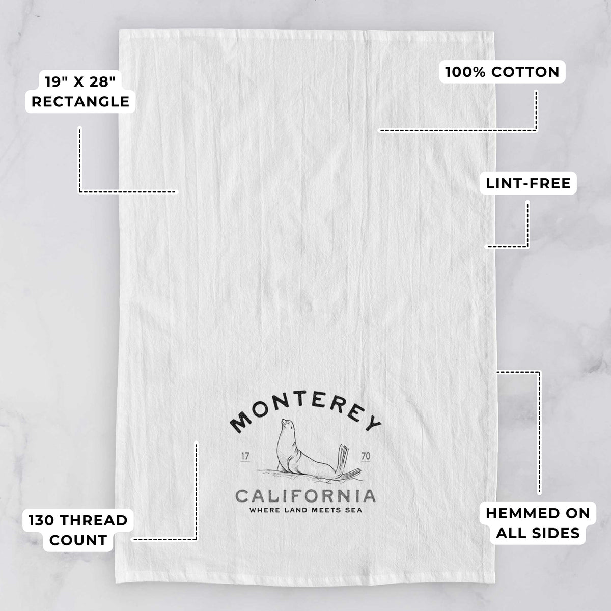 White tea towel printed with a black ink sea lion with the words Monterey California, 1770, Where Land Meets Sea, with feature labels: 19 by 28 inch rectangle, 100% cotton, lint-free, 130 thread count, hemmed on all sides.