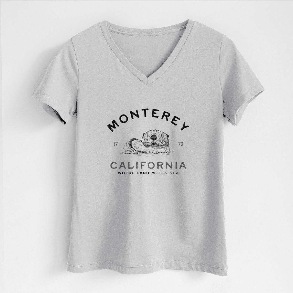 Lunar grey women's relaxed fit cotton V-neck t-shirt laid flat, printed with a black ink sea otter floating on its back, with the words Monterey California, 1770, Where Land Meets Sea.