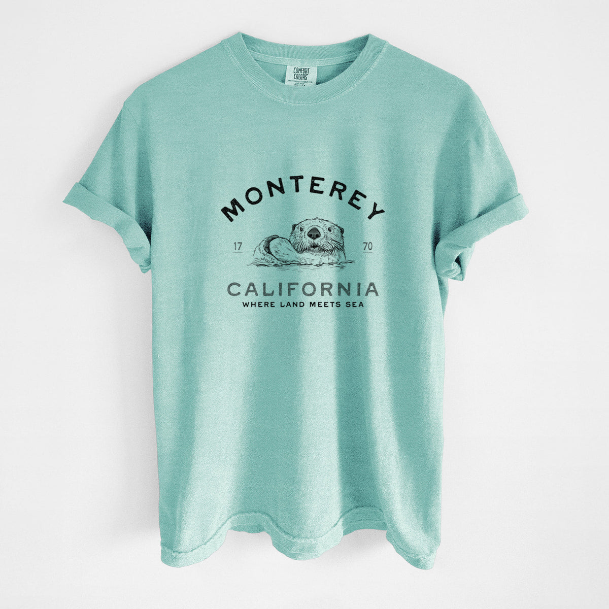 Chalky mint Comfort Colors t-shirt laid flat, printed with a black ink sea otter floating on its back, with the words Monterey California, 1770, Where Land Meets Sea.
