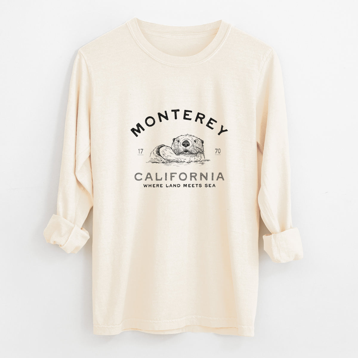 Ivory Comfort Colors long sleeve shirt laid flat with the cuffs rolled, printed with a black ink sea otter floating on its back, with the words Monterey California, 1770, Where Land Meets Sea.